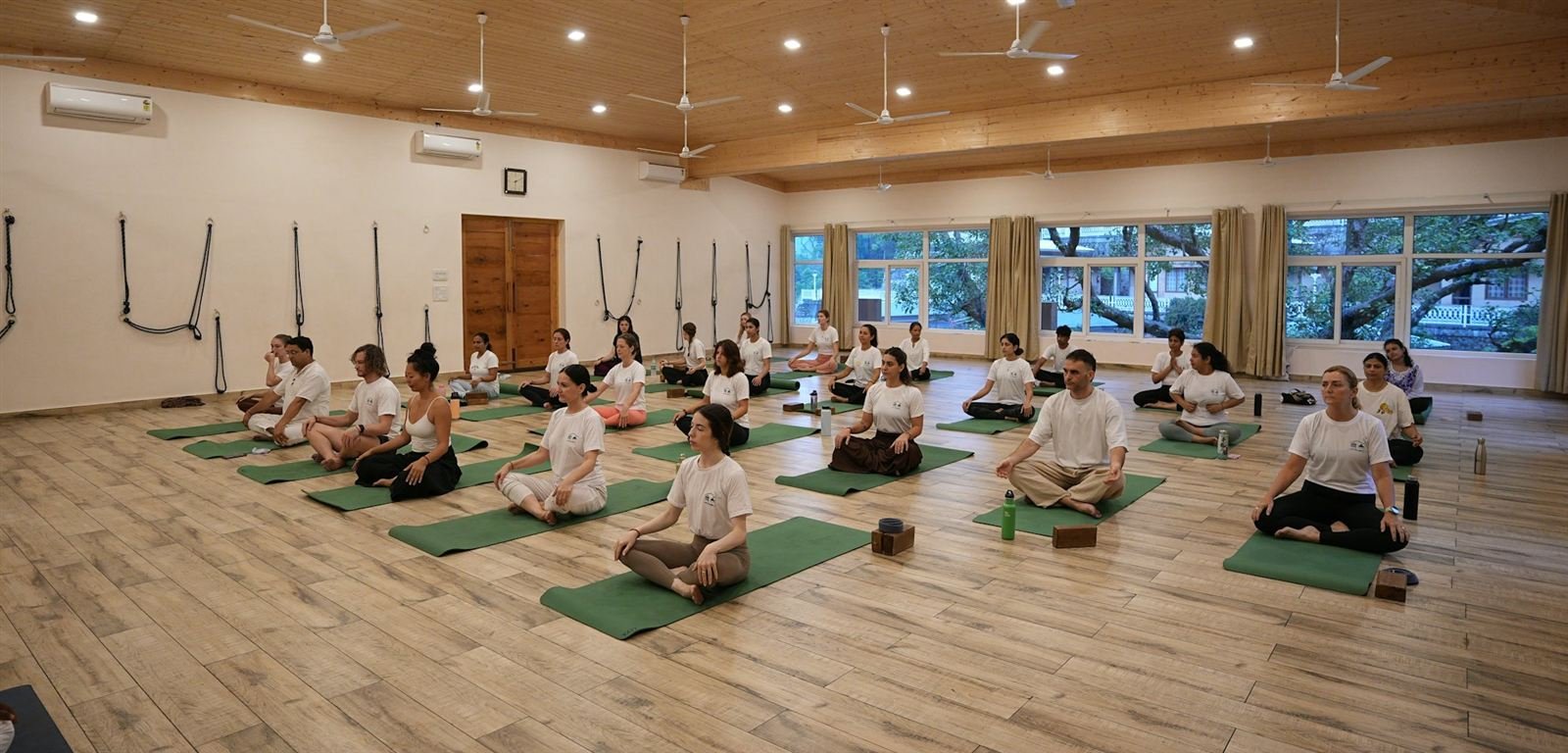A yoga class sitting cross-legged on mats in a bright wooden studio