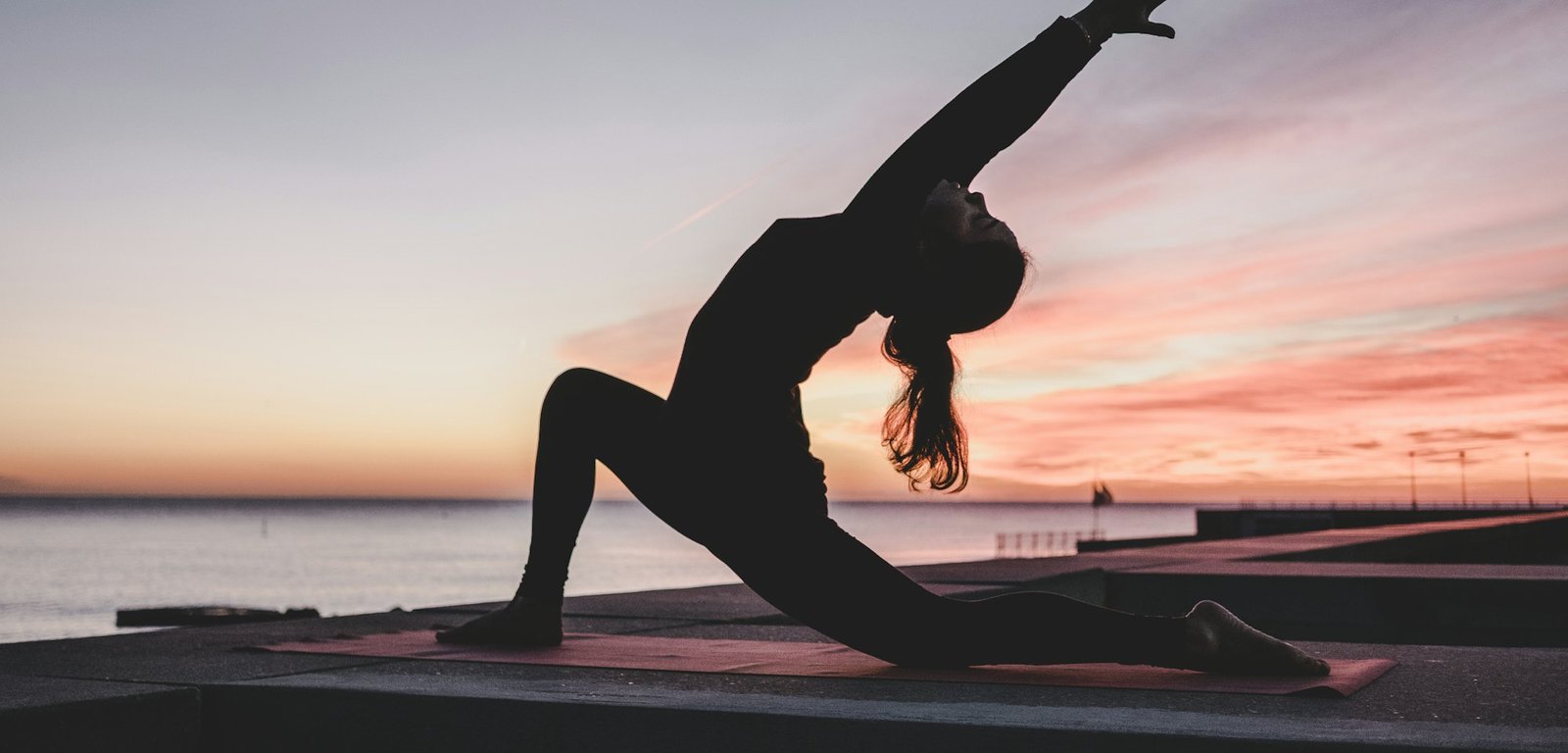 Silhouette of a woman in a crescent lunge at sunset by the sea