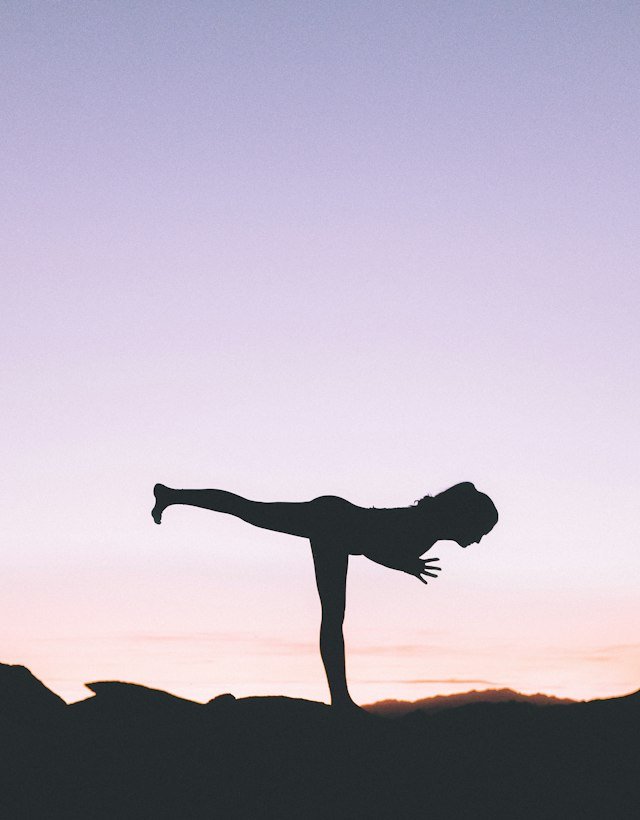 Silhouette of a woman balancing in warrior three against a pink sky
