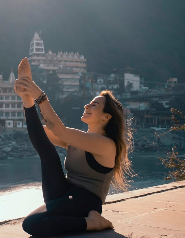 A woman practising a seated leg stretch on a riverside terrace in India