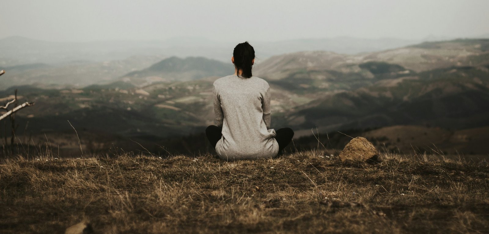 A woman sitting on a cliff edge looking out over misty mountains