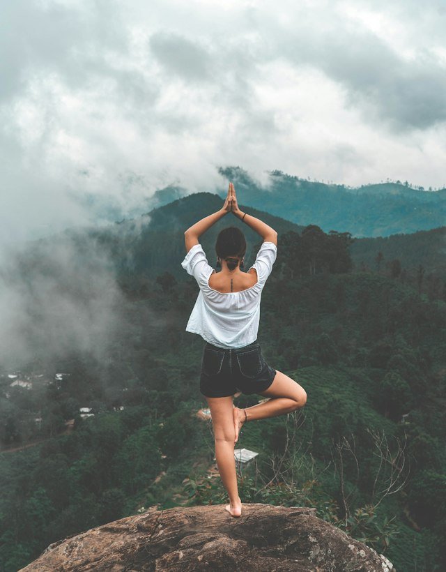 A woman in tree pose on a misty mountain top